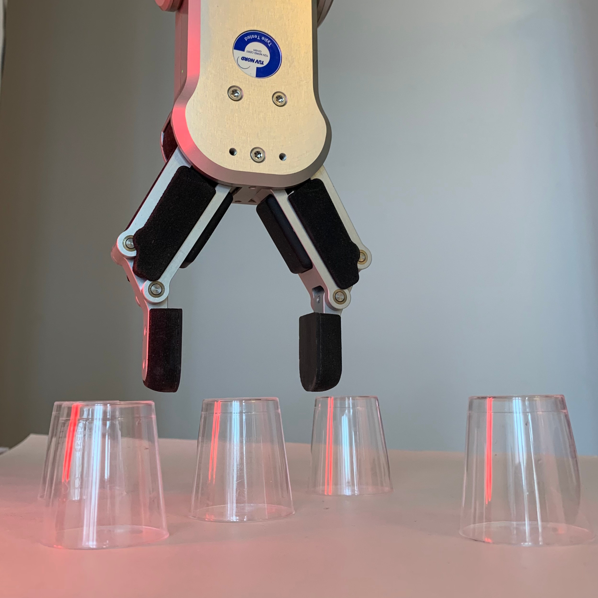Robotic gripper positioning above a row of transparent cups